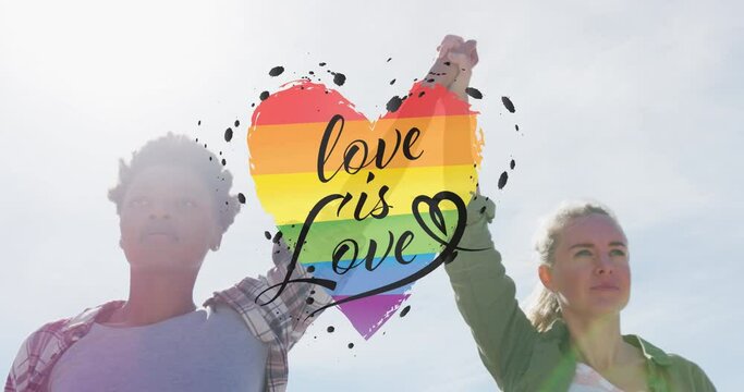 Animation of rainbow heart and love is love over lesbian couple holding hands outdoors
