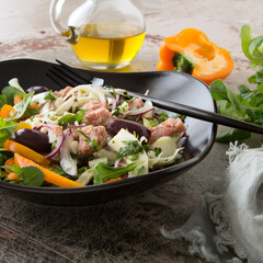 a plate of tuscan salad with tuna, fennel, peppers and olives on the table
