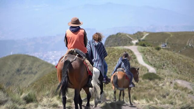 Tourists are riding horses on a trail of Rucu Pichincha near Quito Ecuador. They are wearing ponchos.