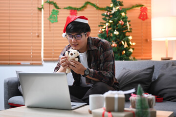 Young asian man in Santa hat holding teddy bear and having video call with his daughter.