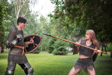 Battle of a fantasy warrior girl and a medieval knight in full set armor in the park.