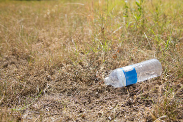 Empty clear plastic bottle dumped  on dry waste ground with weeds