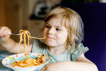 Adorable toddler girl eat pasta spaghetti with tomato bolognese with minced meat. Happy preschool...