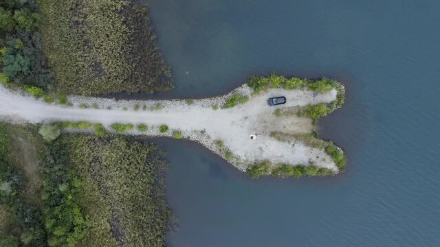 White sanded penisula in a lake with a picnicing coucle and a parked car from above - time for romance