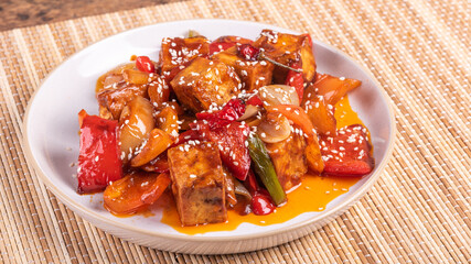 Stir fry tofu with onion and pepper in hot sauce on a plate - asian vegetarian cuisine