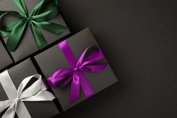 Top view photo of three stylish black gift boxes with purple green and white satin ribbon bows on isolated black background with copyspace