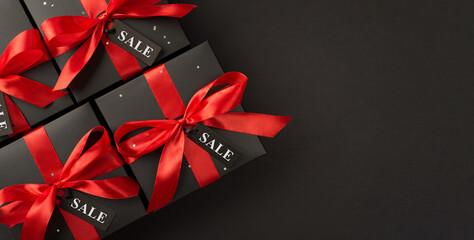 Top panoramic view photo of black gift boxes with red satin ribbon bow on isolated black background with copyspace