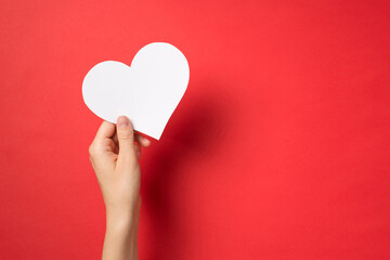 First person top view photo of hand holding white paper heart on isolated red background with copyspace