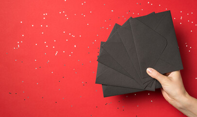 First person view above photo of female hand holding pile of black envelopes isolated on the red background with confetti
