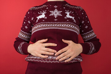Cropped closeup photo of girl in red and white christmas sweater holding her hurting stomach on...