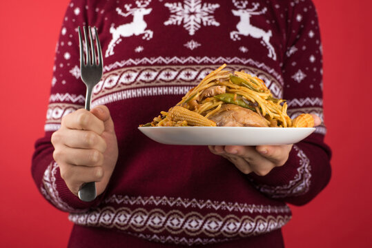 Cropped closeup photo of girl in red and white christmas sweater holding large plate of food and fork on isolated red background
