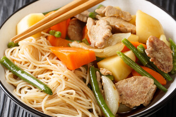 Nikujaga is made from thinly sliced meat stewed with potato, carrot and onions in a slightly sweet soy based sauce close up in bowl on the wooden table. Horizontal