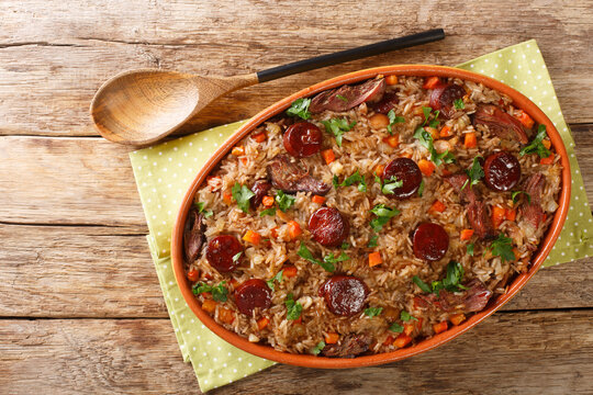 Authentic Arroz de pato duck rice is a traditional recipe from Portugal cooked with red wine, onion, carrot and chorizo close up in the baking dish on the wooden table. Horizontal top view from above