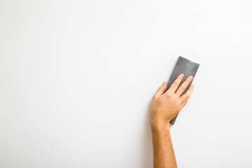 Young adult man hand polishing white wall with sanding sponge. Closeup. Copy space. Empty place for text.