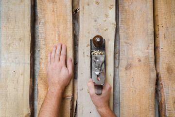 Young adult man hands using jointer and shaving old wooden floor planks. Closeup. Preparing for repair work of home. Flooring restoration. Top down view.