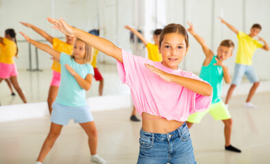 Fototapeta premium Positive girl exercising in group of classmates during dance class at school