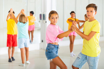 Interested modern tween boy and girl practicing dynamic boogie-woogie in pair during group class in dance studio for children.
