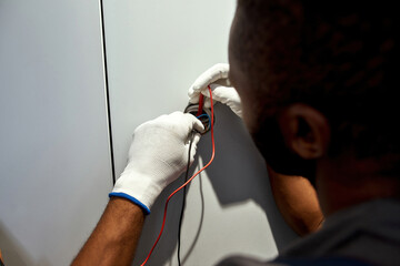 Electrician with tester checking wall socket voltage