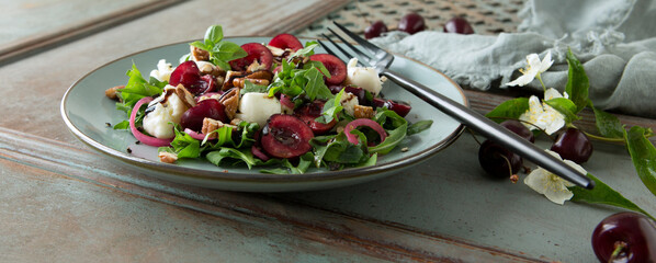 a plate of salad with arugula, mozzarella, nuts and cherries on a wooden table