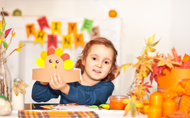 Little cute girl made paper turkey hat for celebrating Thanksgiving day. Diy craft art project.