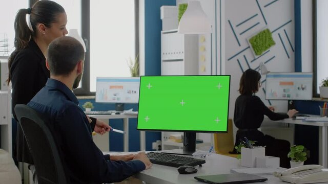 Workmates looking at desk with green screen on monitor for business project. Colleagues discussing marketing plan and strategy while using computer with chroma key and mockup template