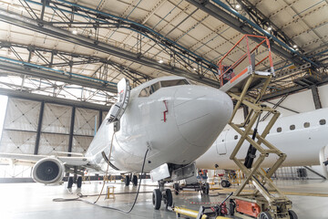 Big white plane with open door and ladder stands beside it in the airport hangar. Aircraft concept