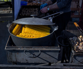 Healthy street food to go: Lots of yellow corn cobs cooked in a large cauldron over an open fire....
