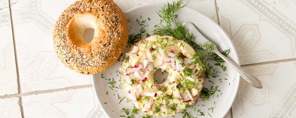 plate with bagel with butter and radishes on a light table