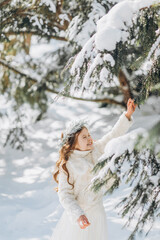 Little girl shaking the branch of pine tree covered by snow.