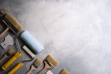 Spatulas for application of putty and brushes and rollers for painting on a gray concrete background.Top view
