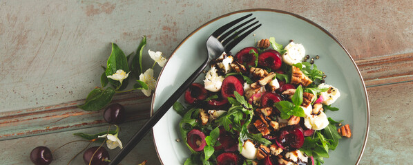 a plate of salad with arugula, mozzarella, cherries and nuts on a wooden table