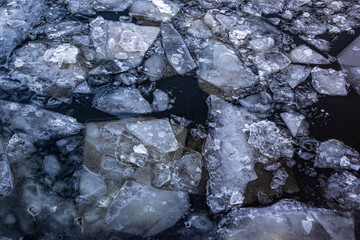 Broken ice of dark blue color on the river. Chunks of crushed ice on dark water. Abstract ice background. Blue background with cracks on the ice surface. Cracks of frozen water