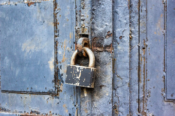 A blue old wooden door with a rusty steel lock. Farm gate from planks with an old padlock. The lock on the door of the shed. Reliable old barn rusty padlock on a wooden door