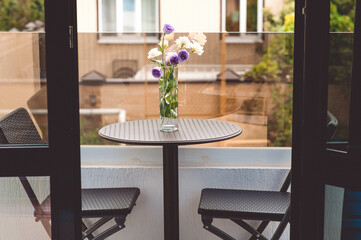 There is a dining table on the terrace and a beautiful bouquet on the table. On the sides of the table and two chairs.