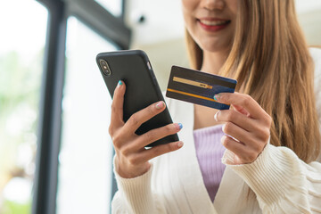 Young beautiful Asian woman using smartphone and credit card for online shopping at home with copy space. E-payment technology, shopaholic lifestyle, or mobile phone financial application concept