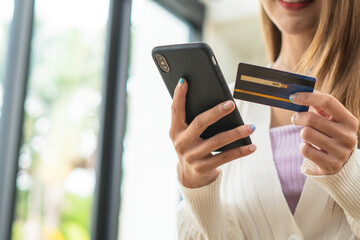 Young beautiful Asian woman using smartphone and credit card for online shopping at home with copy space. E-payment technology, shopaholic lifestyle, or mobile phone financial application concept
