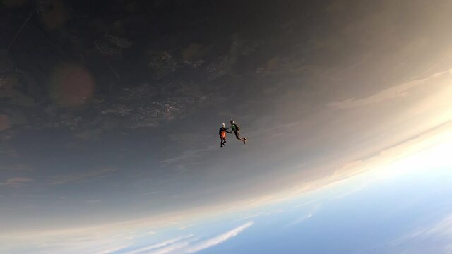 Freefly skydiving. Two guys are flying headdown in the sunset sky. Slow motion.