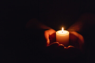 Hands holding burning candle in dark like a heart.Selective focus,black background.Copy space.