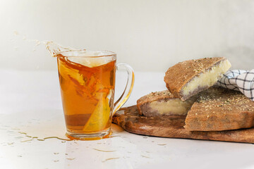 Glass cup and splashes of delicious tea with lemon and vegan vegetable pie on a wooden board