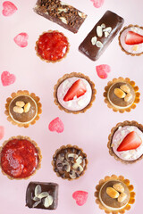 Raw vegan cupcakes and chocolate bars with pink jelly candy hearts on light pink background. Top view.