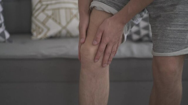 Knee pain, man suffering from ache and doing self-massage at home, self-soothing massaging