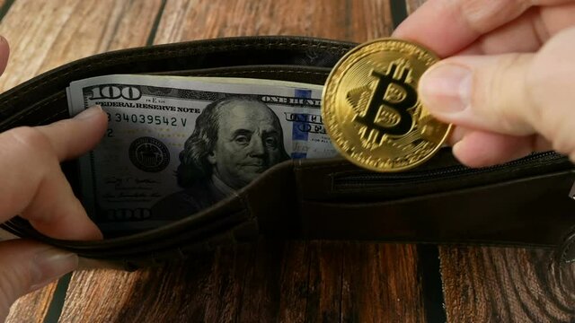 hand takes out the golden bitcoin from wallet with american dollars on wooden background, multicurrency concept