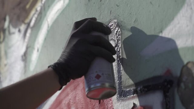 Close up shot of a hand wearing black gloves painting graffiti on wall. Artist drawing black line in a grafiti with a spray paint