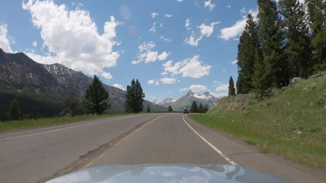 POV Driving a car on asphalt road in Montana mountains leading to Yellowstone National Park. Blue sky on sunny day	