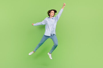 Fototapeta na wymiar Full body photo of happy cheerful cool woman jump up raise hand super hero empty space isolated on green color background