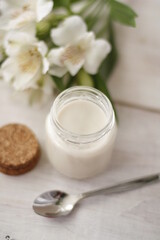 Obraz na płótnie Canvas Glass jar with white creme or yoghurt with spoon and flowers flatlay