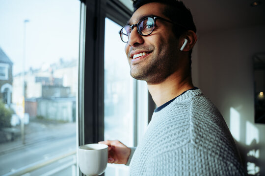 Smiling mixed race business man working from home enjoying hot morning coffee listening to music with earphones