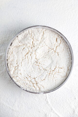 Flour in round metal bowl and scattered around on background. Flour texture background.