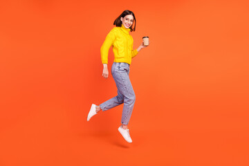 Full size profile side photo of young woman happy smile jump up drink coffee isolated over orange color background