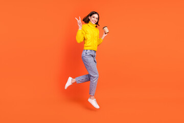 Fototapeta na wymiar Full body profile side photo of young woman happy positive smile jump show peace v-sign drink tea isolated over orange color background